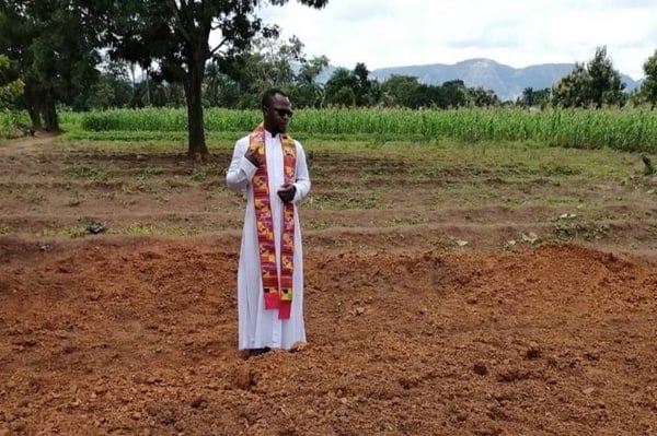 Father Etube prays over mass grave