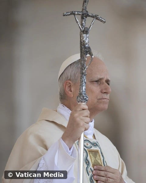 Pope Leo XIV holding the papal cross, hand over his heart, in prayer